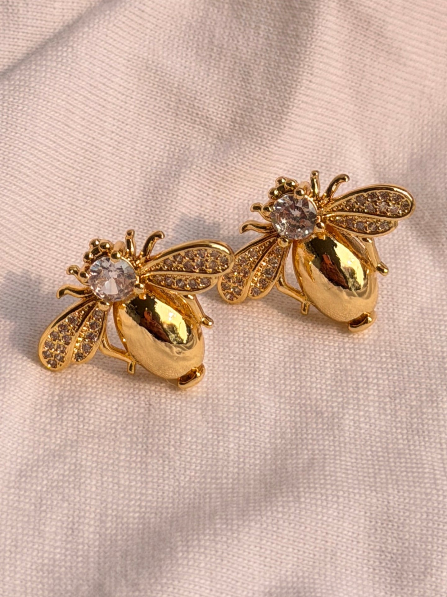 Gold bee-shaped earrings on a light fabric background with flowers.
