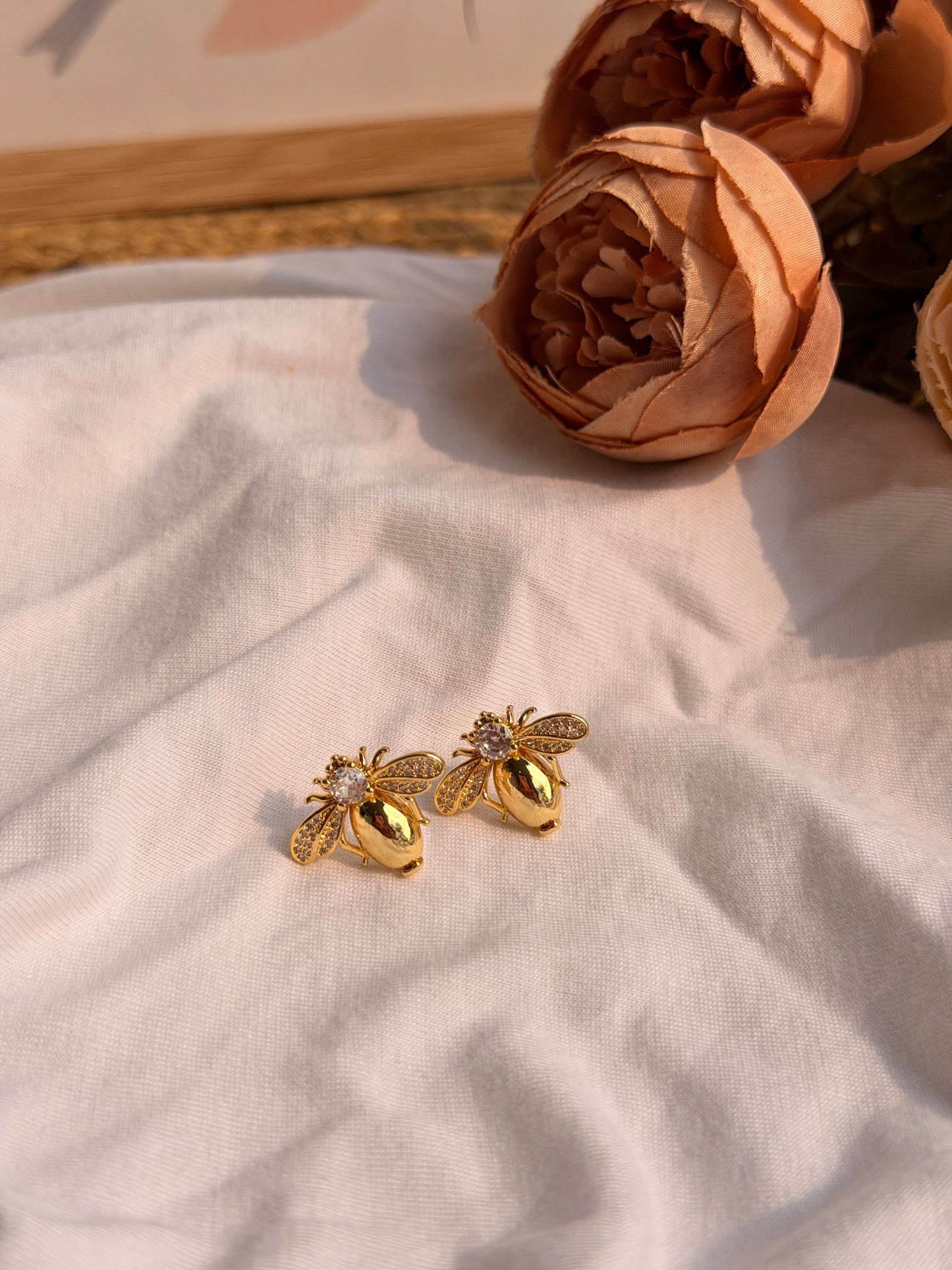 Gold bee-shaped earrings on a light fabric background with flowers.