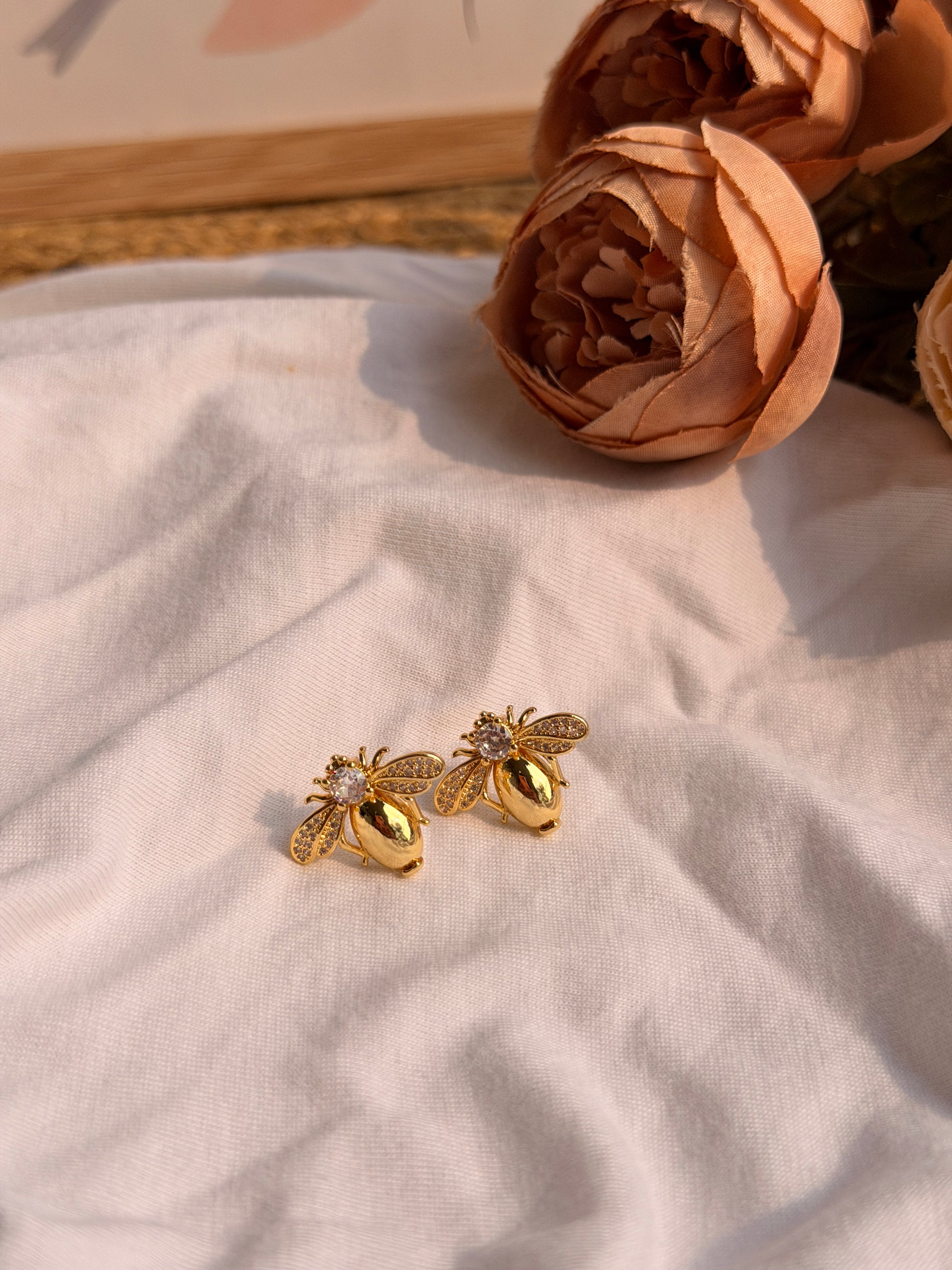 Gold bee-shaped earrings on a light fabric background with flowers.